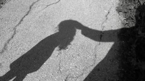 Black and white illustrative image showing the shadows of a child and adult