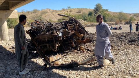 Residents look at the wreckage of a burnt passenger bus in Lasbela district of Pakistan's Balochistan province on 29 January