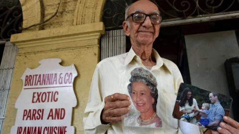 Indian restaurator Boman Kohinoor, 93, an ardent fan of the British royal family, poses with photos of Queen Elizabeth, and the Duke and Duchess of Cambridge outside the Britannia & Co. restaurant in Mumbai on April 8, 2016,