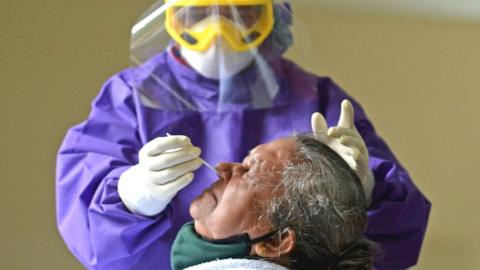 A medical worker wearing Personal Protective Equipment (PPE) gear collects a swab sample