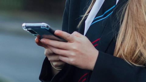 Stock image of a school pupil holding a smartphone