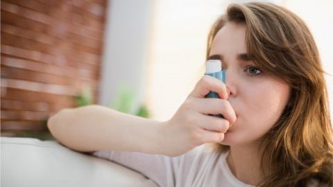 Young woman using her asthma inhaler on a couch