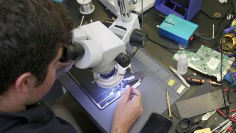 Sam Mencimer looks through a microscope to repair an electrical device