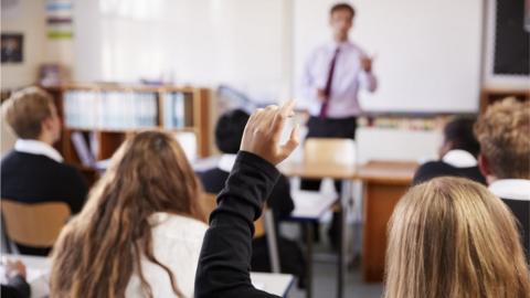 Pupils sit in a classroom with hands raised