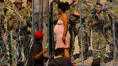 A pregnant woman stands at a security fence installed by the Texas National Guard at the US border with Mexico
