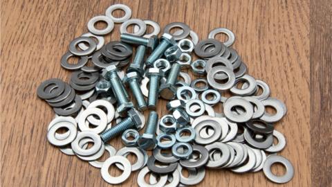 A pile of metal nuts, bolts and washers on a wooden background