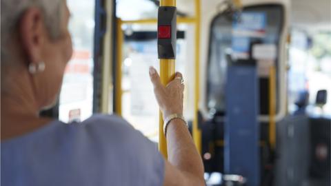 A senior woman on a bus holds a bar with a stop button on it