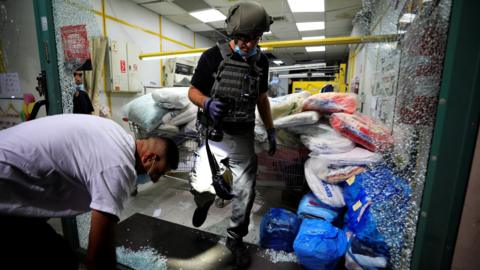 Israeli security personnel inspect a shopfront damaged in a rocket attack on the Israeli city of Ashdod (15 September 2020)