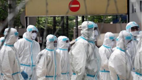 Police officers wearing protective suits gather outside an apartment under enhanced lockdown to pick up illegal immigrants in Kuala Lumpur (1 May 2020)