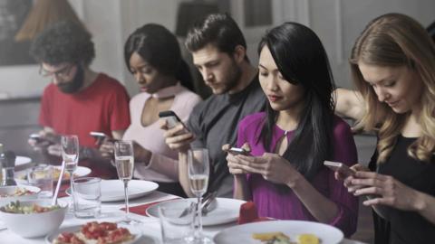 Group of adults sit at dinner on mobile phones