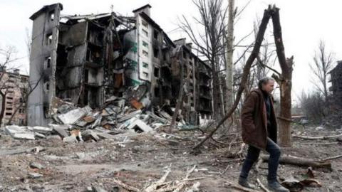 A man walks by a residential building destroyed in the southern port city of Mariupol