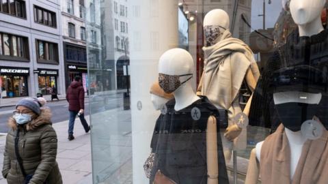 Woman walks past shop with masked dummies in window