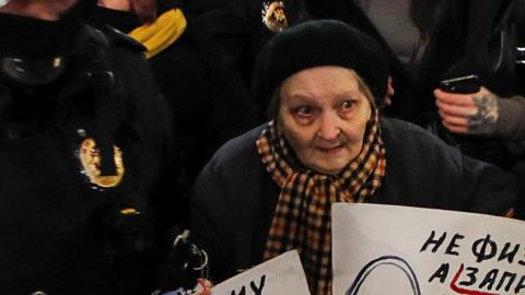 Law enforcement officers escort an elderly woman during an anti-war protest