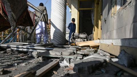 People inspect a damaged house after several rockets land at Khair Khana