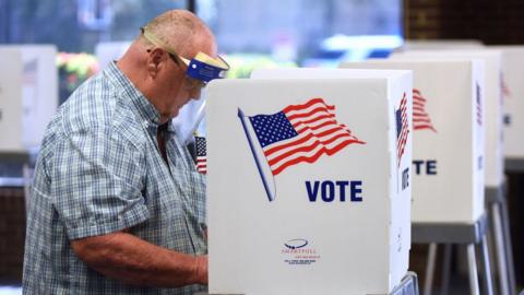 A man in a face shield casts his vote