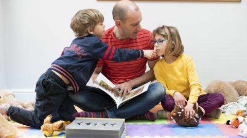 Roger Whalley reads to his son Wolf and daughter Josie while she sniffs the scent kit