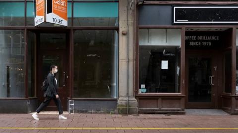 A woman walking along Cardiff street with empty shops behind