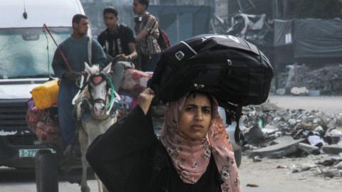 A Palestinian woman carries her belongings as she flees Jabalia, in the northern Gaza Strip (12 May 2024)
