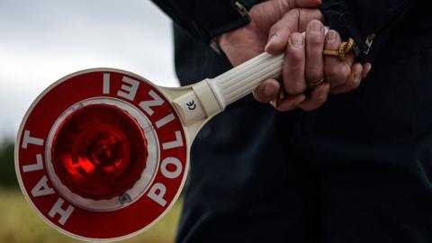 A German police man holds a stop sign reading, "Halt, Polizei"