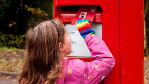 Child posting a letter into a postbox