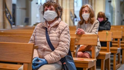 Three women with masks on praying