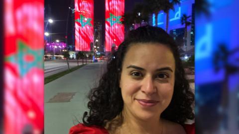 BBC journalist Lina Shaikhouni takes photo in front of two towers with the Moroccan flag projected on them.