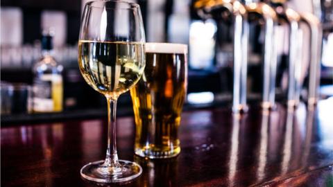 A wine glass and pint of beer on a bar