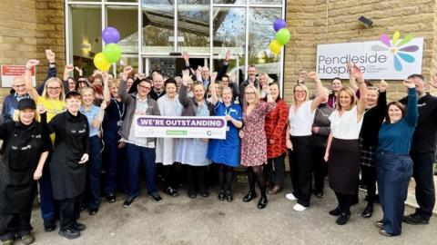Pendleside Hospice holding a banner saying outstanding to celebrate its CQC rating