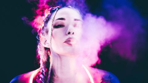 A young woman vaping under neon light