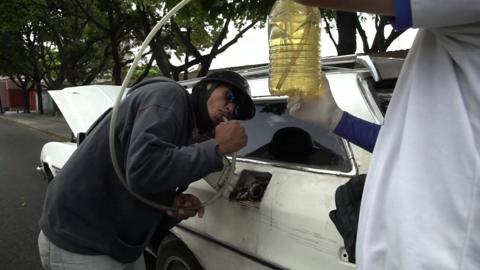 A man siphons fuel into a car