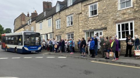 A crowd of people lining up for a bus that is being cut