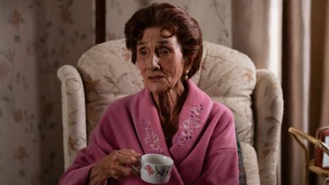 June Brown as Dot Branning in EastEnders, sitting in an armchair drinking a cup of tea