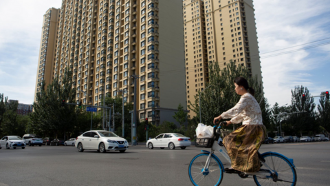 A woman rides a bicycle past an Evergrande housing complex in China's capital Beijing on 28 September 2023