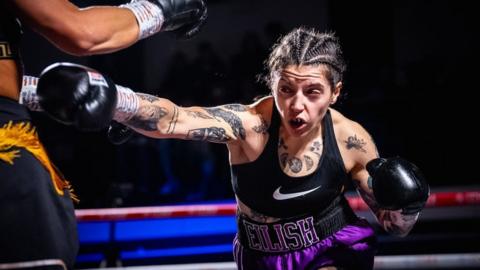 Eilish Tierney throwing a punch, in black gloves, and black vest and purple shorts.