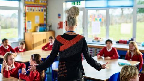 Primary school teacher standing with arms out, preparing children for meditation class - stock photo