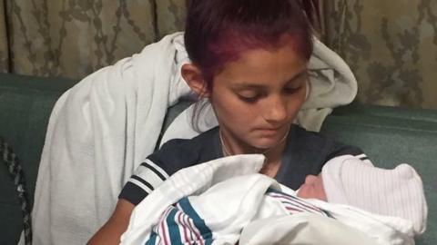 Jacee, back in her civilian clothes, holds her new baby brother