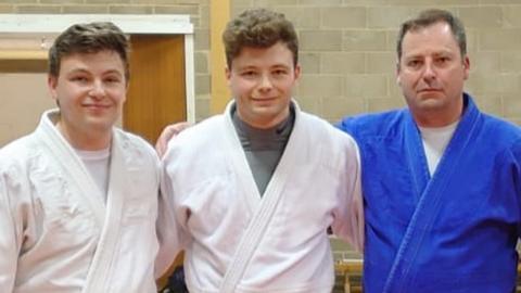 Aaron Hawkins posing for a photo after winning his blackbelt with his brother and father