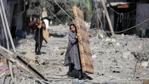 Palestinians walk through debris along a street in the aftermath of Israeli bombardment in al-Karama district in Gaza City