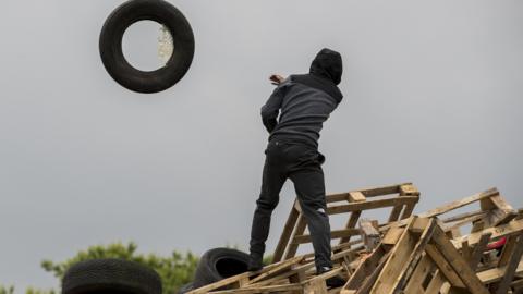 A man throws a tyre from a bonfire at Avoniel Leisure Centre