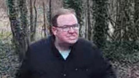 CCTV footage of a white man wearing a wearing glasses, a dark jacket and light blue t-shirt