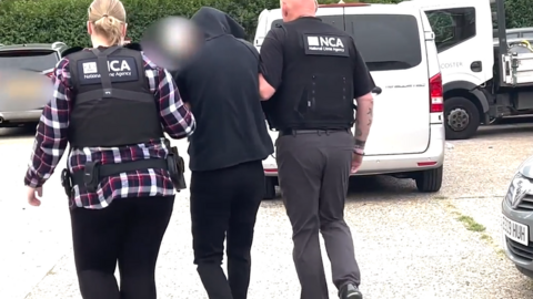 A man is seen being led away in handcuffs following a raid by the National Crime Agency targeting suspected people smugglers