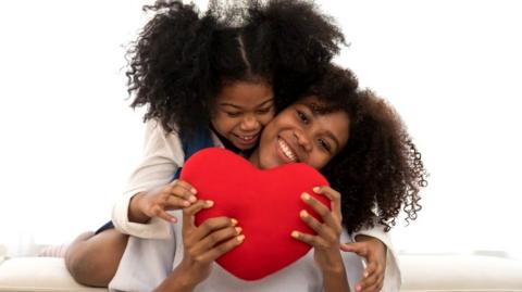 two sisters holding a love cushion