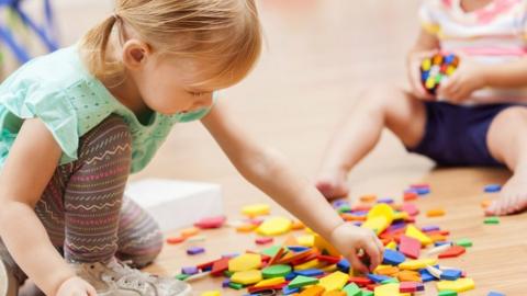 File image showing a young girl playing with coloured blocks on the floor