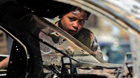 A boy peers through a burnt-out car in Sanaa, Yemen (6 December 2017)