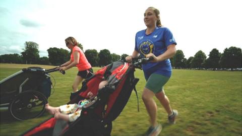 Zoe Jacobs and friend running in a field pushing their babies in prams