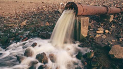 Sewage flowing from a rusty pipe on to a river bank