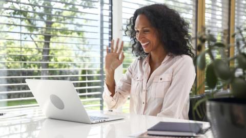 Woman waves to her laptop during a videoconference at home