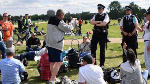 Police speak to a large group gathered in a park in central London