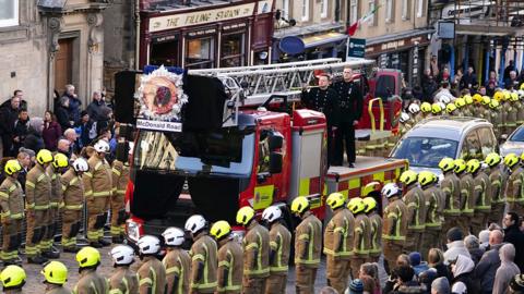 Firefighters line the streets as a coffin passes by