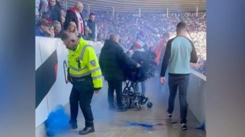 A plume of blue smoke rises into the air after a flare lands in the disabled fans' section at Sunderland's Stadium of Light